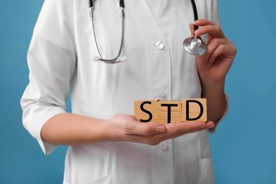 Doctor holding wooden cubes with abbreviation STD on light blue background, closeup