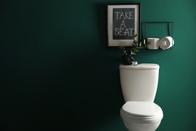 Decor elements, paper rolls and toilet bowl near green wall, space for text. Bathroom interior