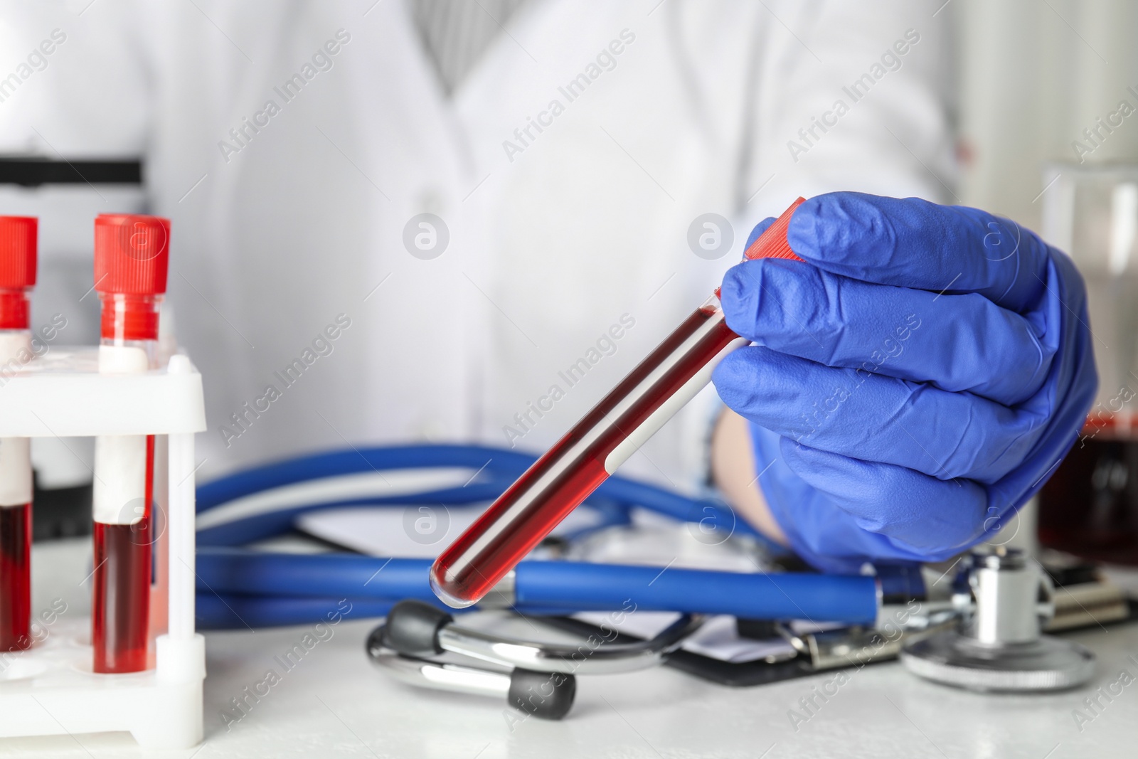 Photo of Scientist holding test tube with blood sample at table, closeup. Virus research