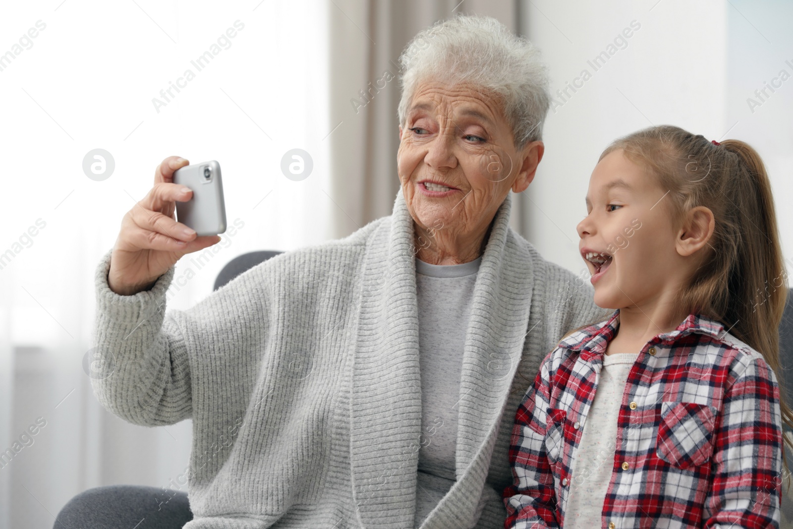 Photo of Cute girl and her grandmother taking selfie  at home