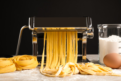 Photo of Pasta maker machine with dough and products on grey table against black background