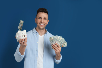 Photo of Happy man with cash money and piggybank on blue background