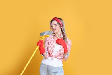 Photo of Beautiful young woman with floor brush singing on orange background