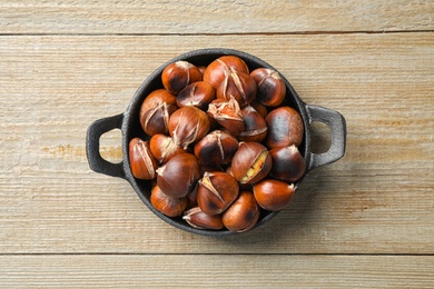 Photo of Tasty roasted edible chestnuts on wooden table, top view