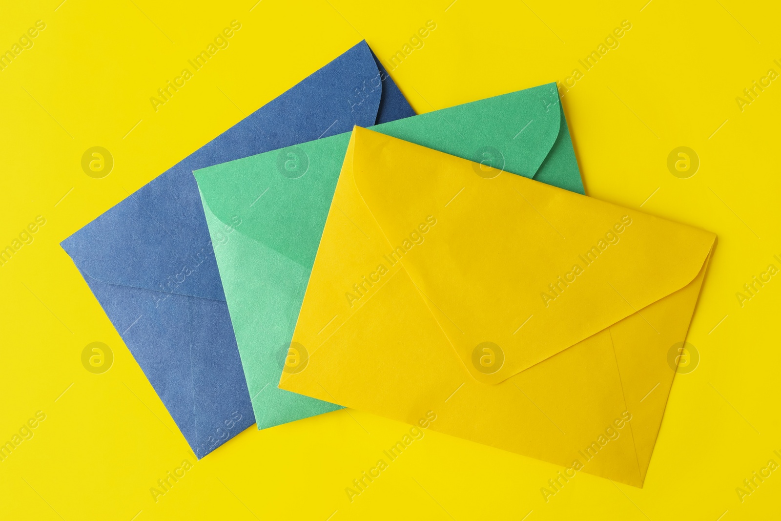 Photo of Colorful paper envelopes on yellow background, top view