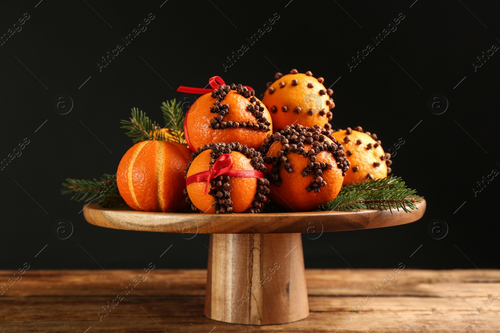 Photo of Pomander balls made of fresh tangerines and cloves on wooden table against black background