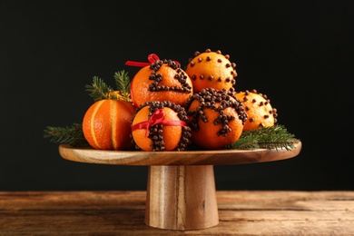 Pomander balls made of fresh tangerines and cloves on wooden table against black background