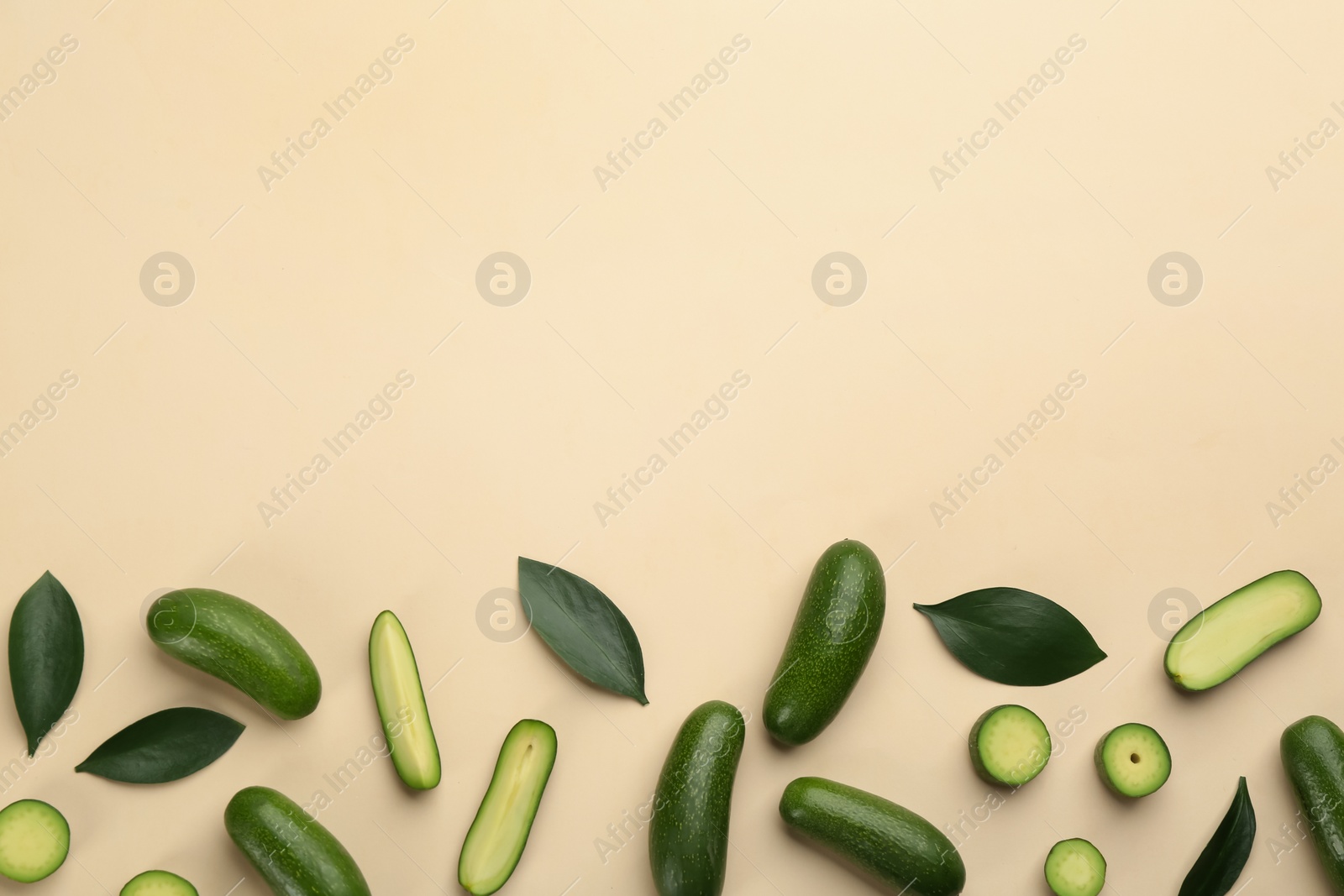 Photo of Whole and cut seedless avocados with green leaves on beige background, flat lay. Space for text