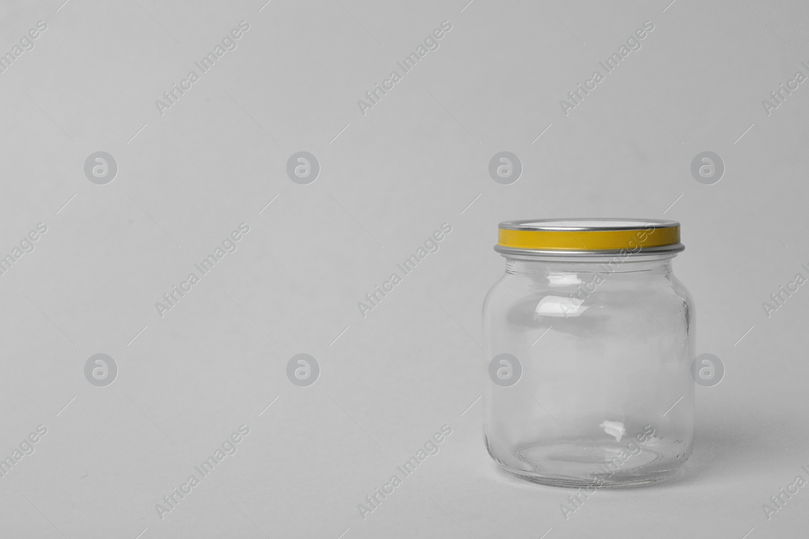 Photo of Closed empty glass jar on light background, space for text