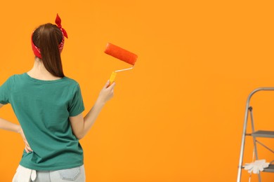 Photo of Designer with roller looking at freshly painted orange wall, back view. Space for text