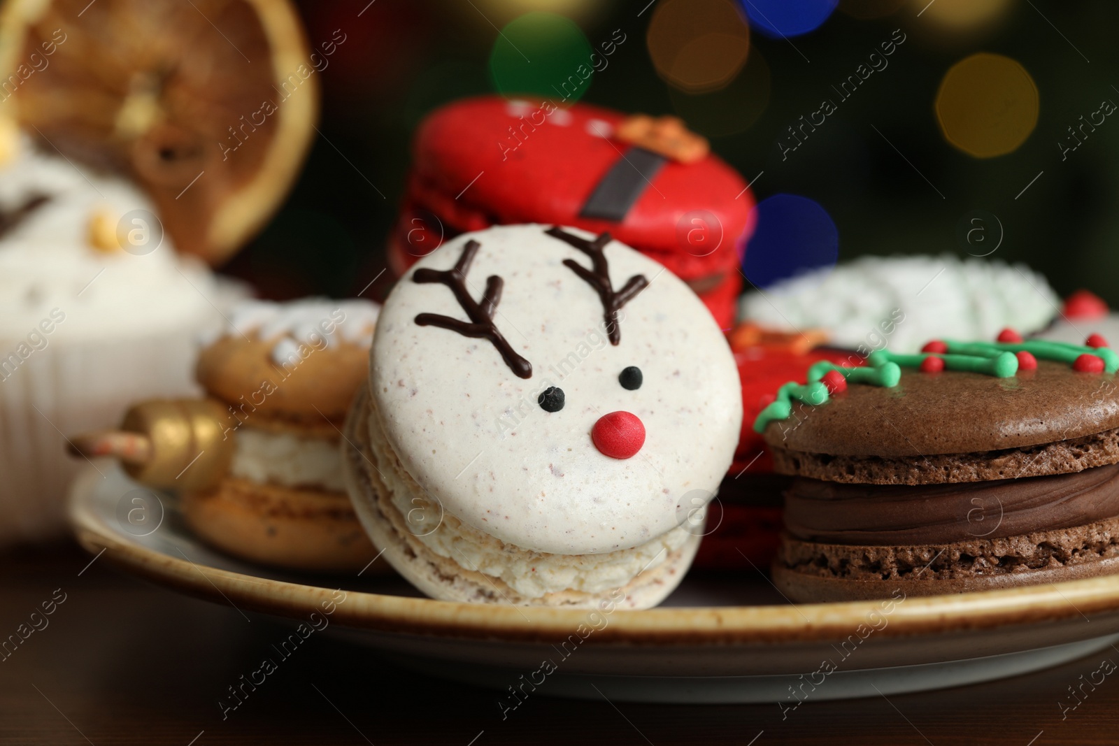 Photo of Beautifully decorated Christmas macarons on wooden table against blurred festive lights, closeup