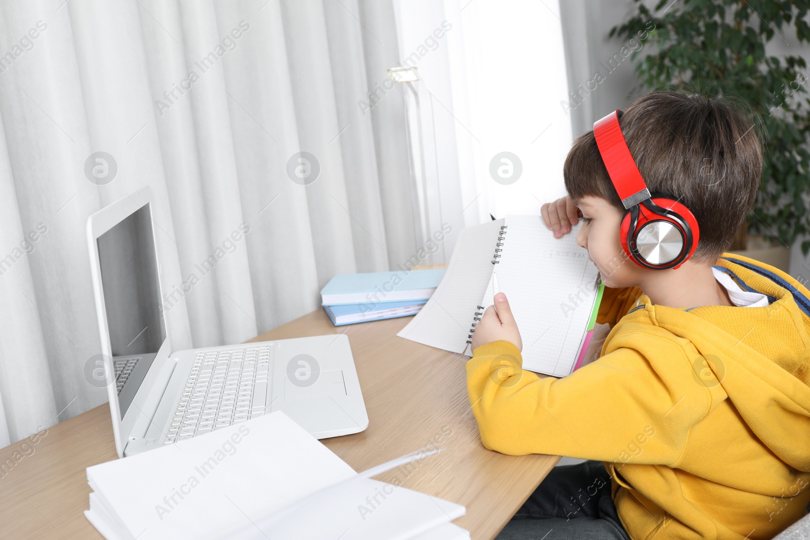 Photo of Cute little boy with modern laptop studying online at home. E-learning