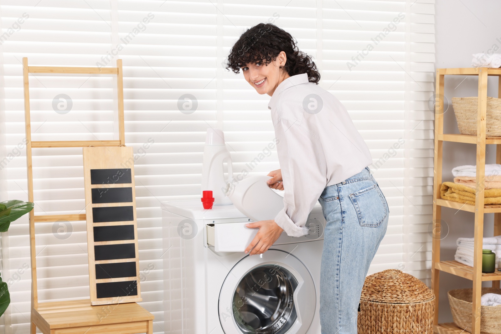 Photo of Woman pouring laundry detergent into washing machine indoors