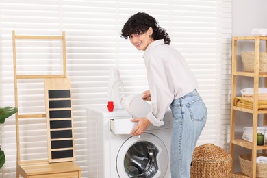 Photo of Woman pouring laundry detergent into washing machine indoors