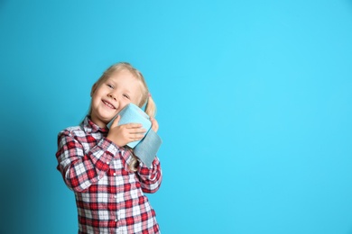 Photo of Cute little girl holding toilet paper roll on color background. Space for text