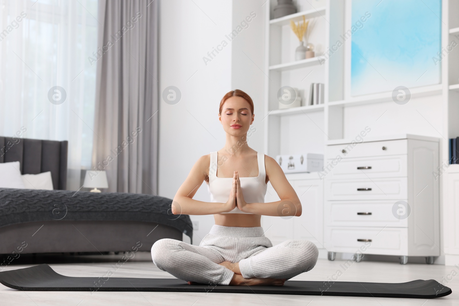 Photo of Beautiful young woman practicing Padmasana on yoga mat at home. Lotus pose