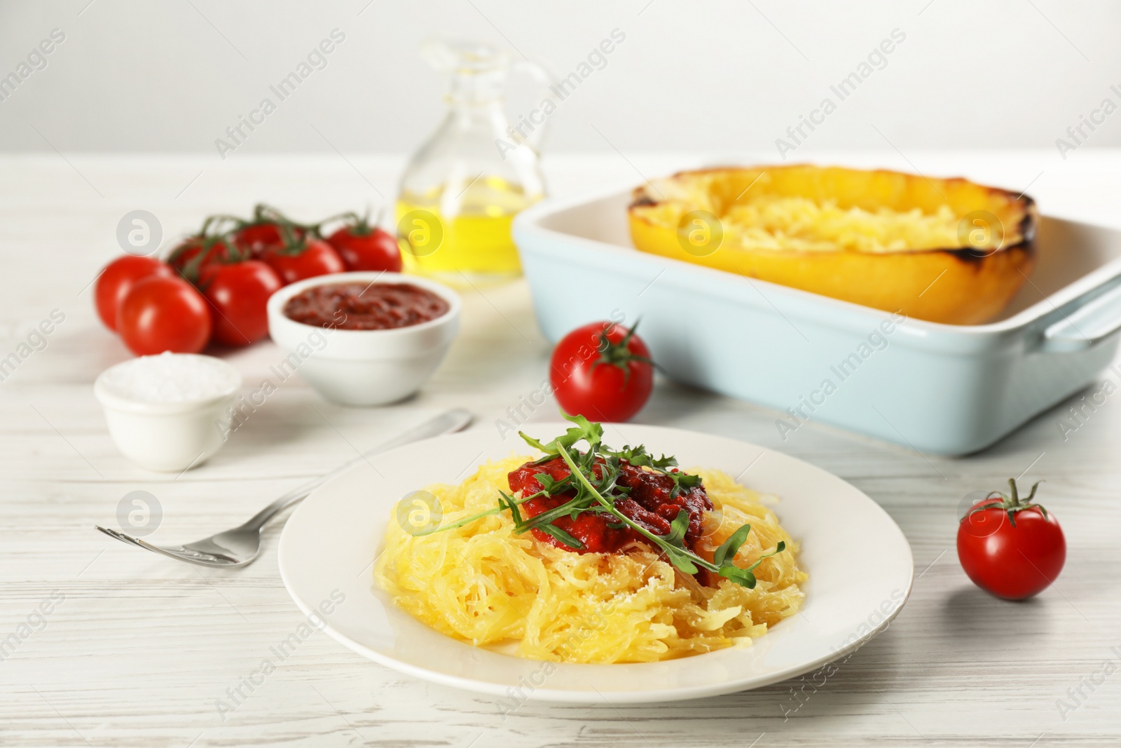 Photo of Tasty spaghetti squash with tomato sauce and arugula served on white wooden table