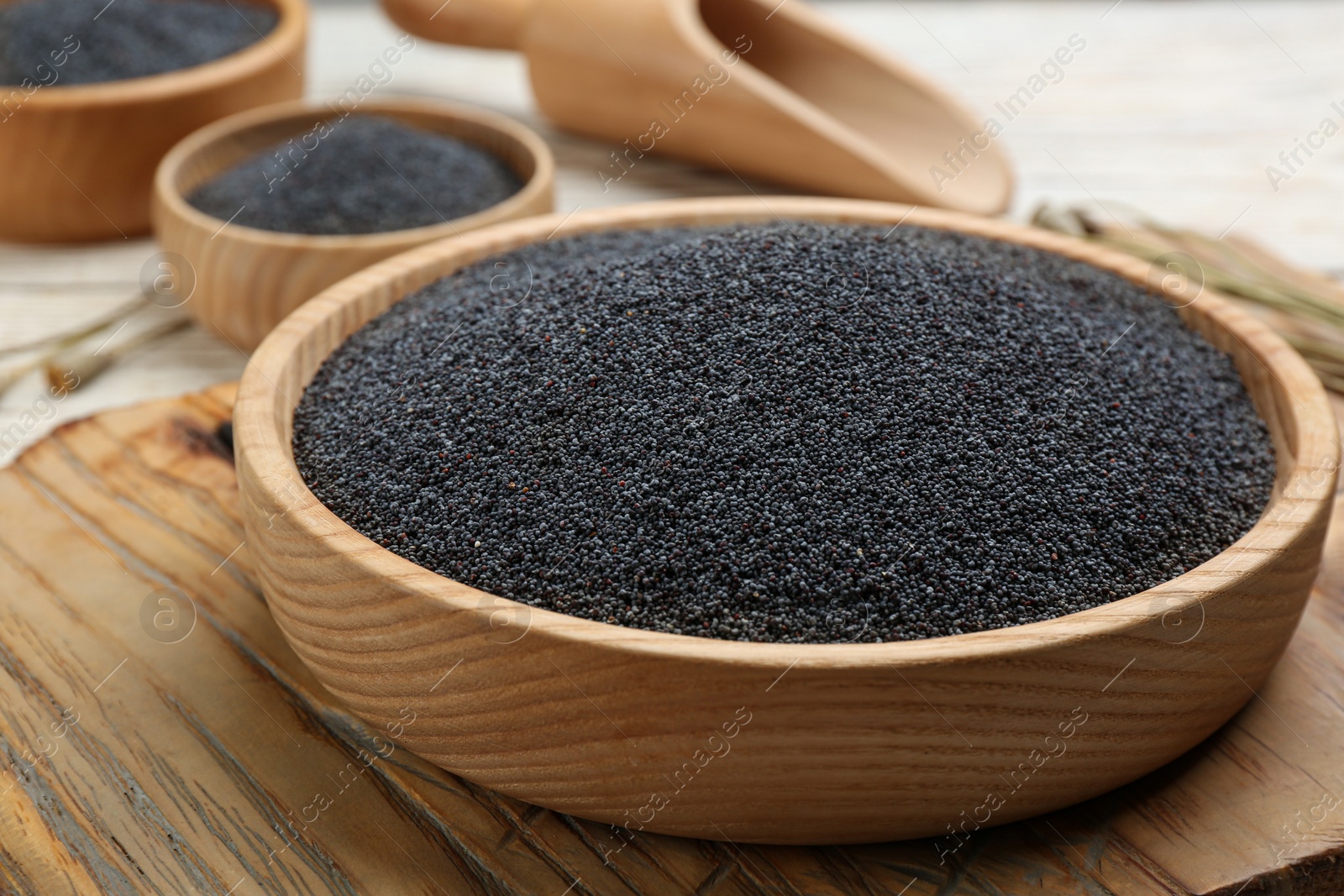 Photo of Poppy seeds in bowl on wooden board, closeup