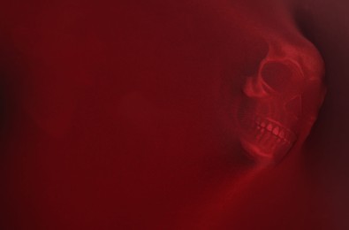 Photo of Silhouette of creepy ghost with skull behind red cloth. Space for text