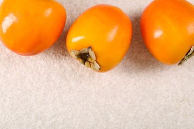 Photo of Delicious ripe persimmons on light textured table, top view. Space for text