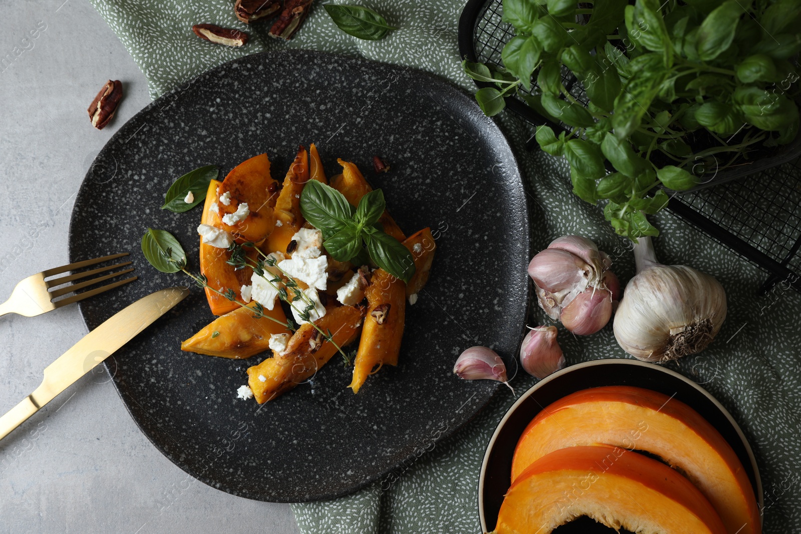 Photo of Baked pumpkin slices served with cheese, thyme, basil and pecans on light table, flat lay