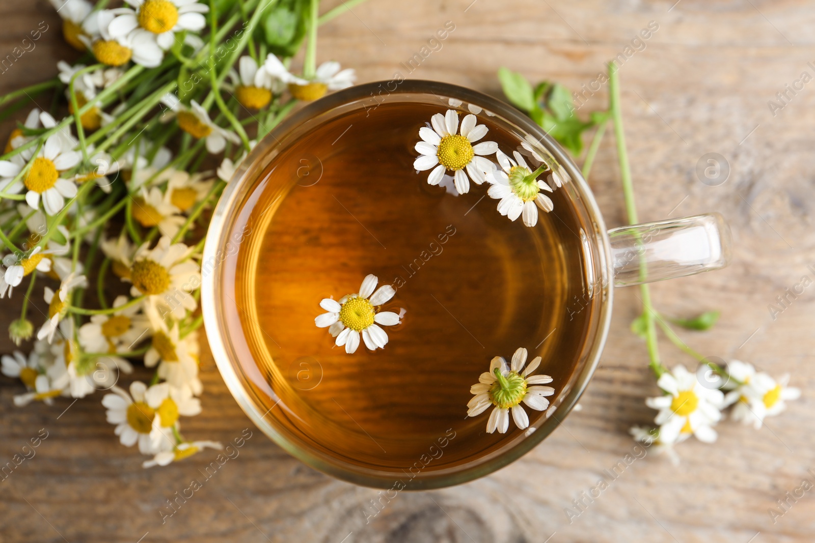 Photo of Cup of tea and chamomile flowers on wooden table, flat lay