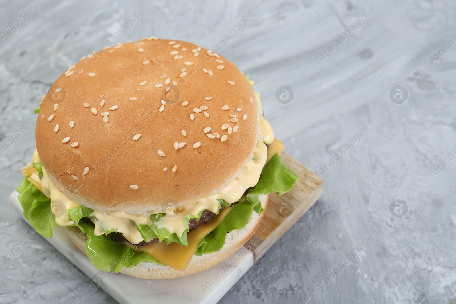 Photo of Delicious cheeseburger on grey textured table, closeup. Space for text