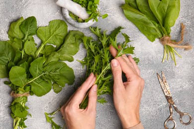 Photo of Woman with fresh green herbs at light grey table, top view