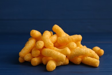 Photo of Heap of tasty cheesy corn puffs on blue wooden table