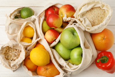 Cotton eco bags with fruits and cereals on white wooden table, flat lay