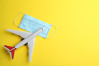 Photo of Toy airplane and protective mask on yellow background, flat lay with space for text. Travelling during coronavirus pandemic