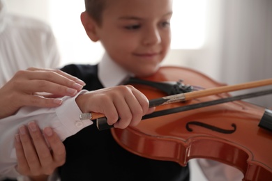 Young woman teaching little boy to play violin indoors, focus on hands