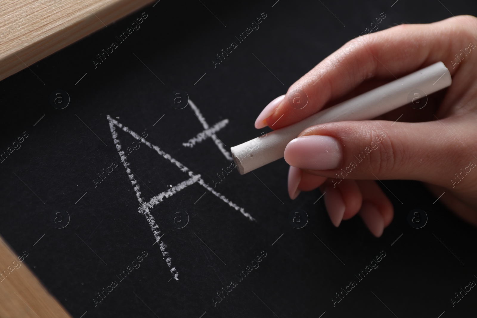 Photo of School grade. Teacher writing letter A and plus symbol with chalk on blackboard, closeup