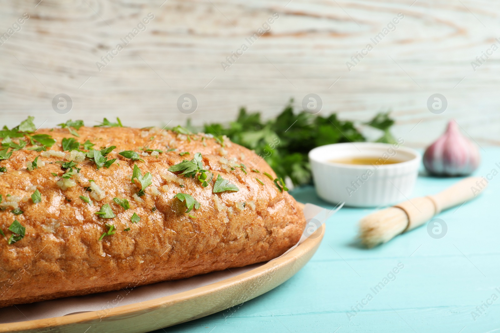 Photo of Loaf of delicious bread with garlic and herbs on light blue wooden table