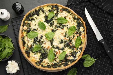 Photo of Delicious homemade spinach quiche and ingredients on black table, flat lay