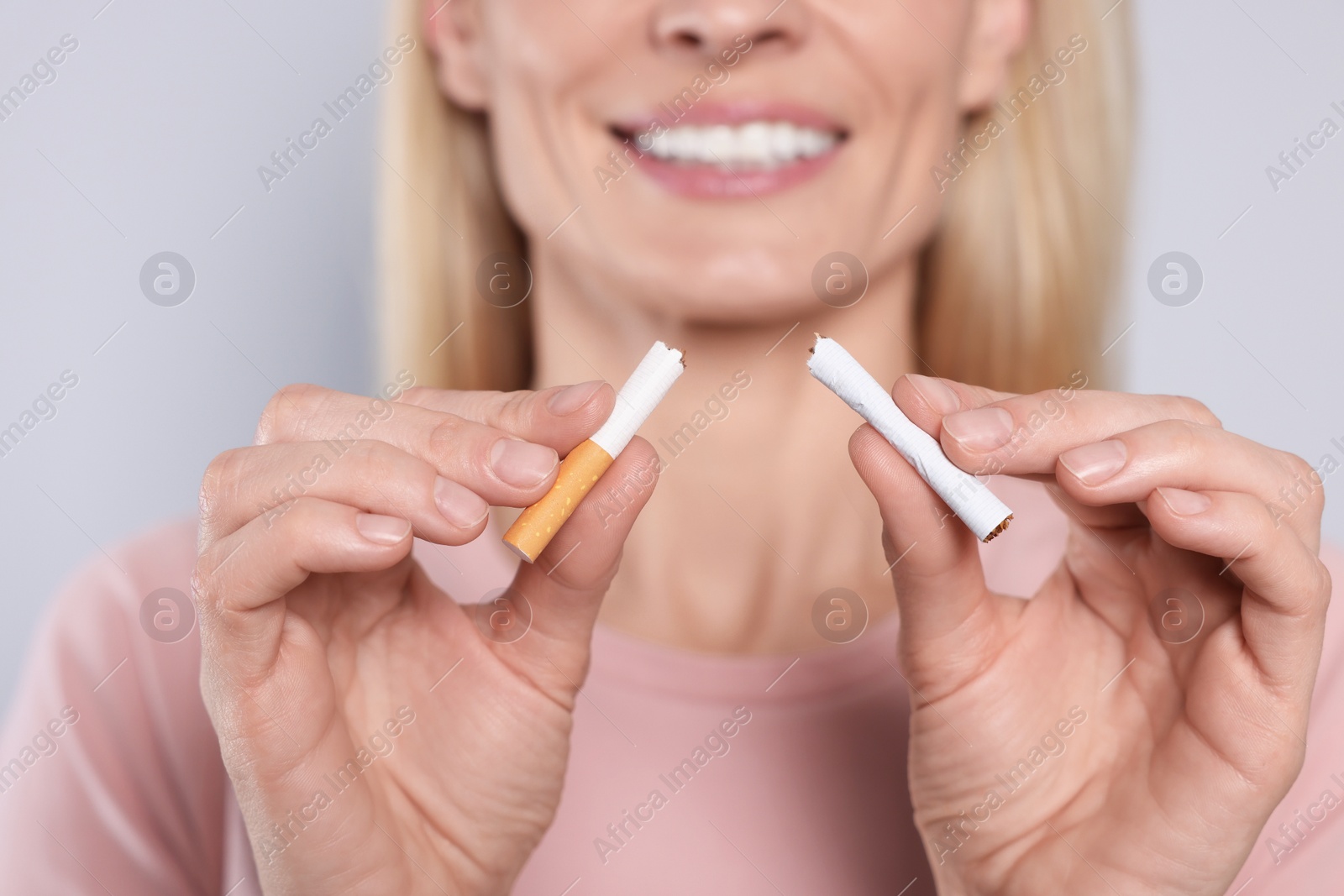 Photo of Woman with broken cigarette on light grey background, closeup. Stop smoking concept