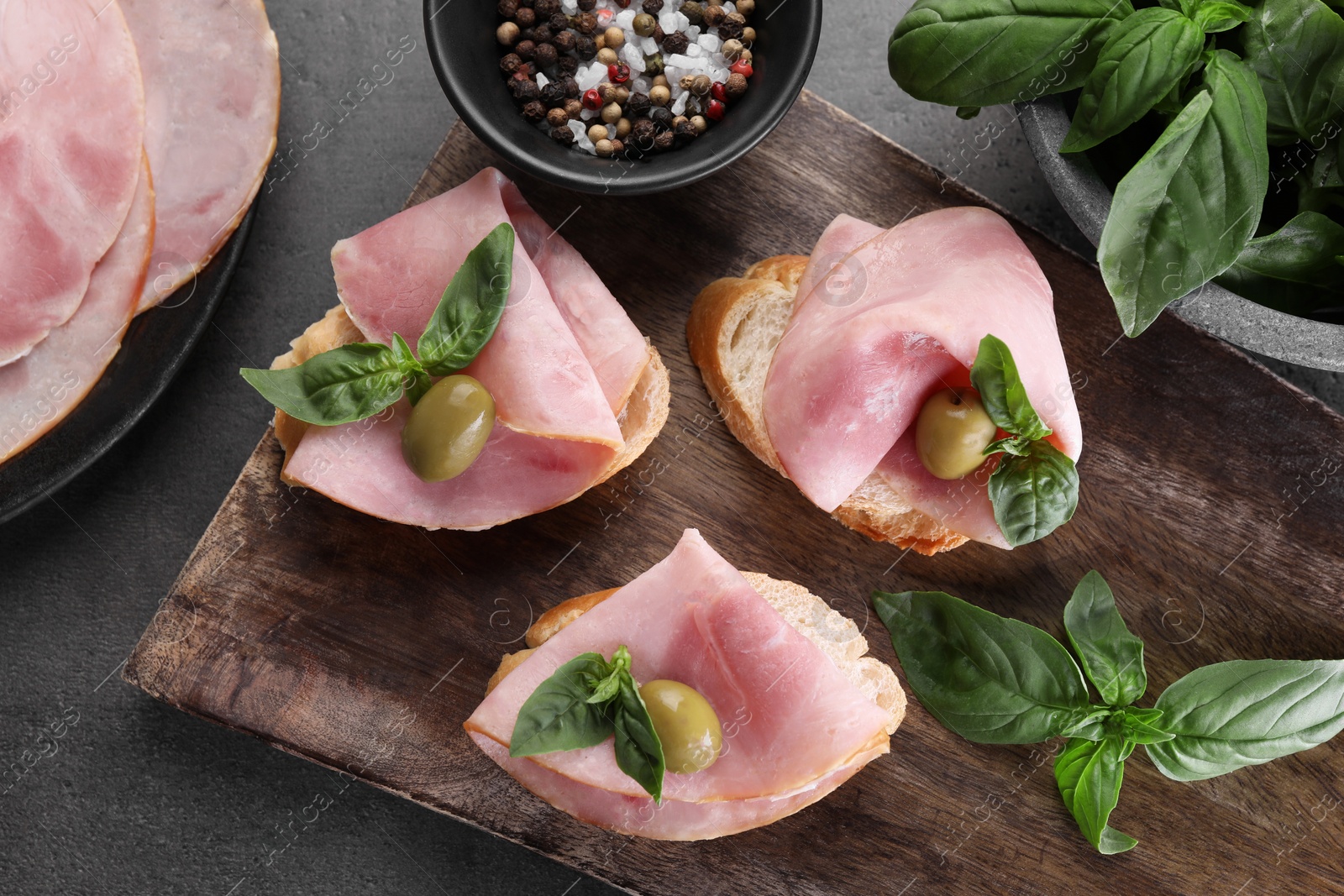 Photo of Delicious sandwiches with ham, basil, olives and spices on grey table, flat lay