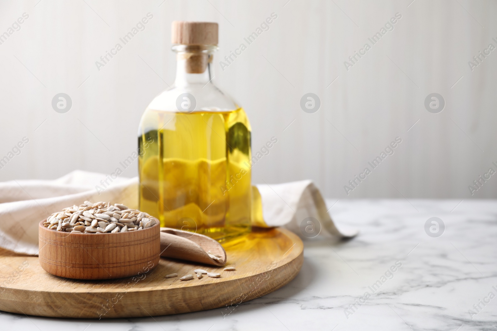 Photo of Sunflower seeds and oil on white marble table. Space for text