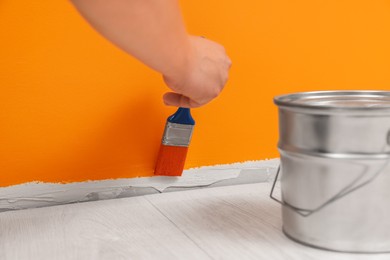 Photo of Worker using brush to paint wall with orange dye indoors, closeup