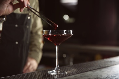 Barman adding cherry into cosmopolitan martini cocktail at counter, closeup. Space for text