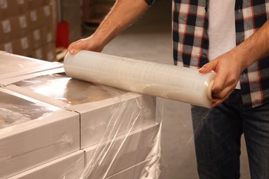 Photo of Worker wrapping boxes in stretch film at warehouse, closeup