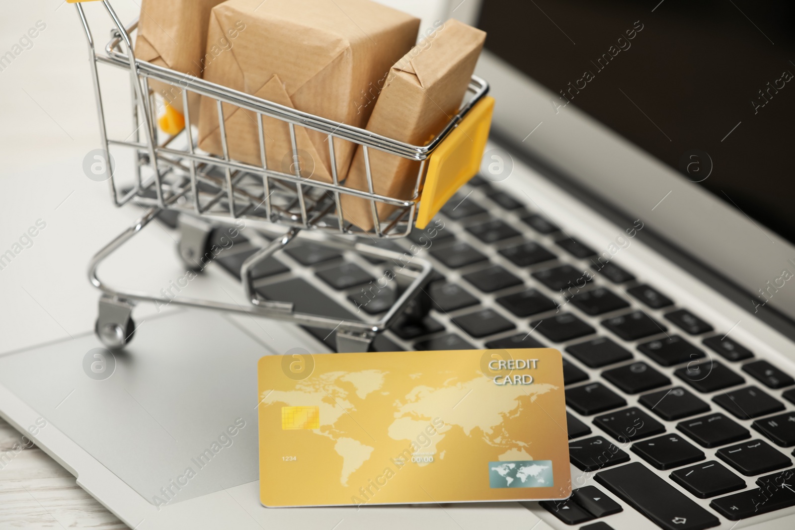 Photo of Online payment concept. Small shopping cart with bank card, boxes on laptop, closeup