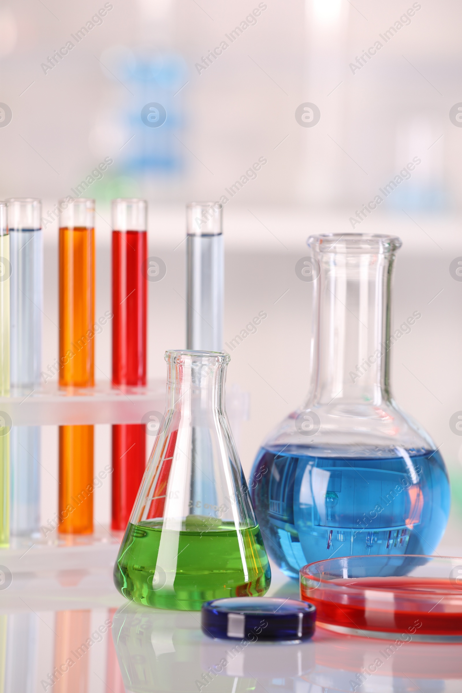 Photo of Laboratory analysis. Glass flasks, Petri dish and test tubes with liquids on white table against blurred background