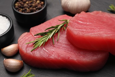 Photo of Fresh raw tuna fillets with rosemary and spices on black table, closeup