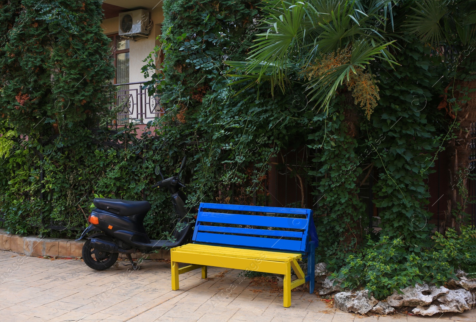 Photo of Beautiful blue and yellow wooden bench near scooter outdoors