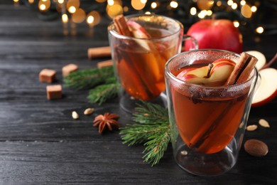 Photo of Aromatic hot mulled cider on black wooden table. Space for text