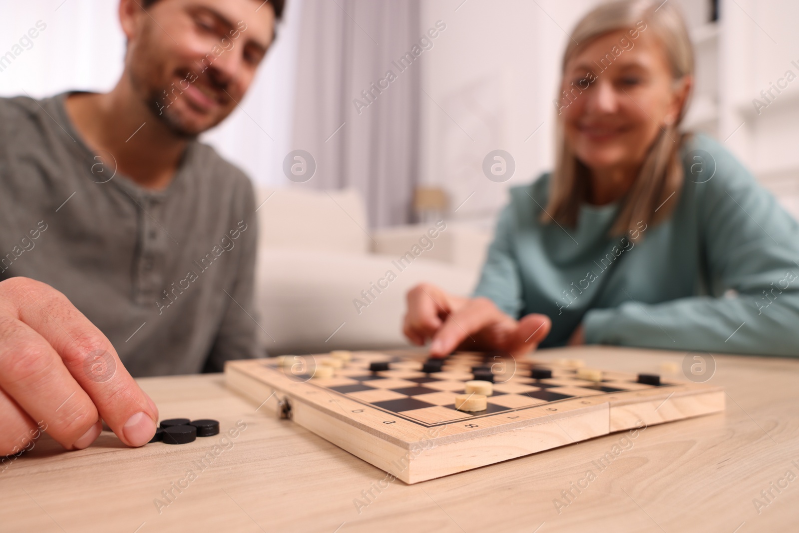 Photo of Family playing checkers at wooden table in room, selective focus