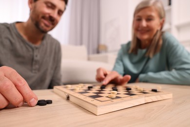 Family playing checkers at wooden table in room, selective focus