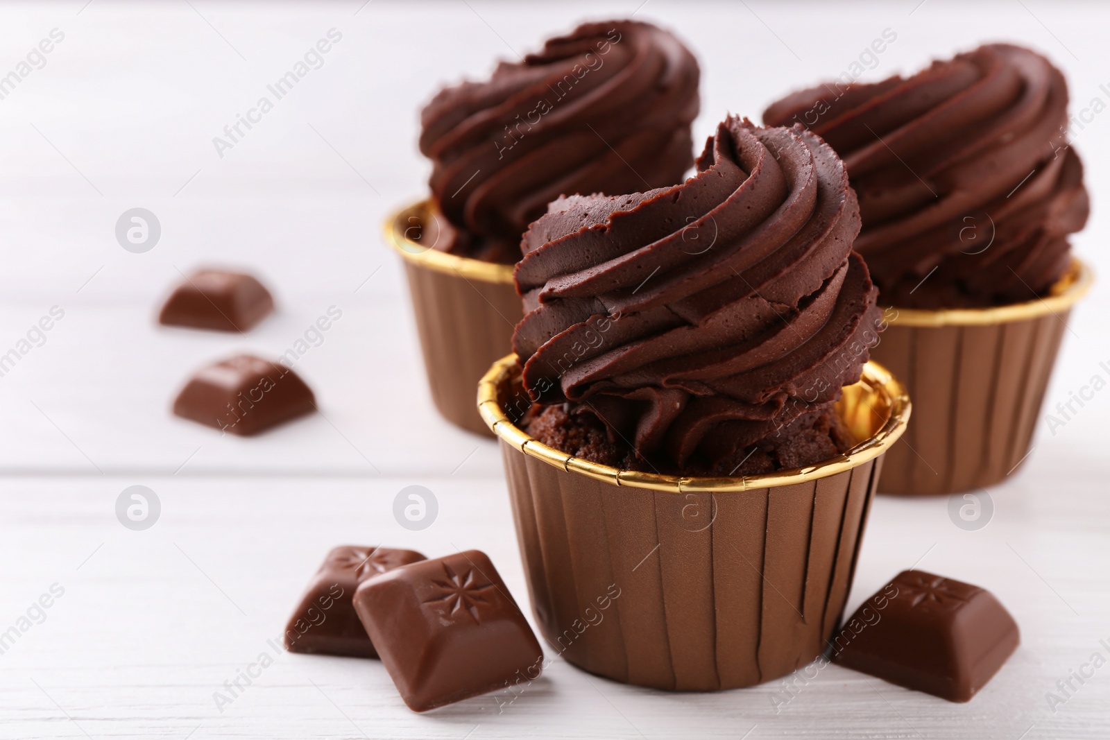 Photo of Delicious cupcakes and chocolate pieces on white wooden table, closeup