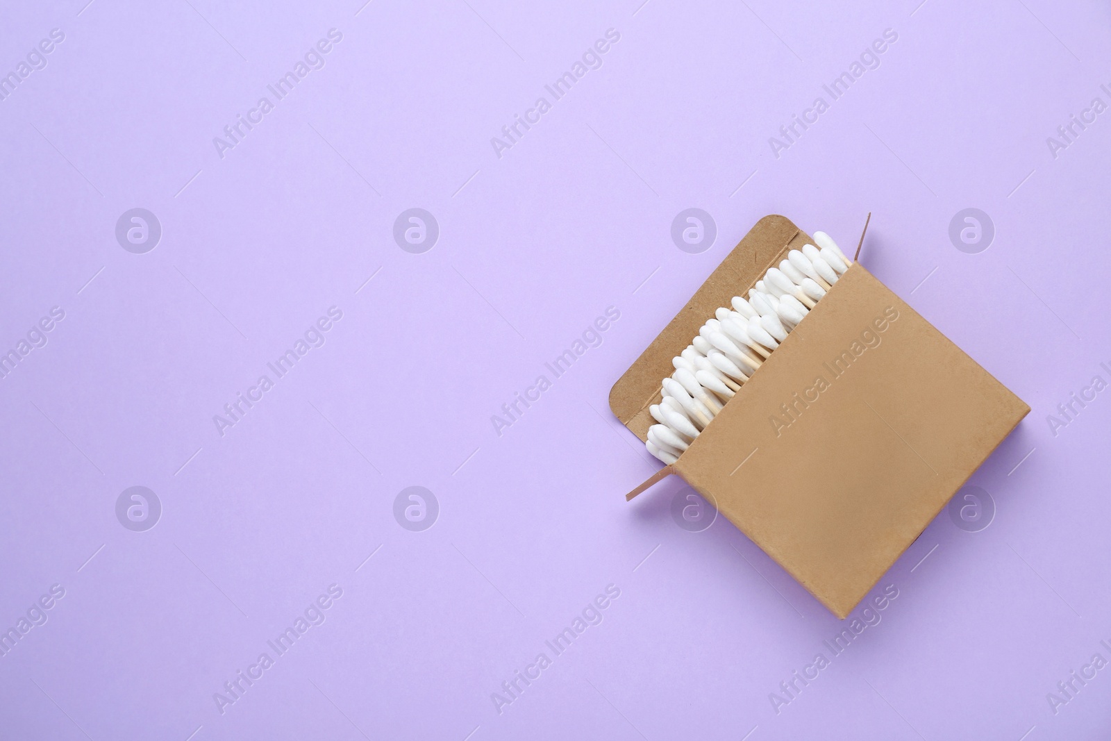 Photo of Box with wooden cotton buds on violet background, top view. Space for text